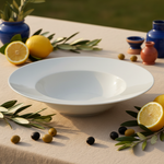 Plato blanco de porcelana para pasta en una mesa mediterránea con lino, aceitunas, limones y ramas de olivo